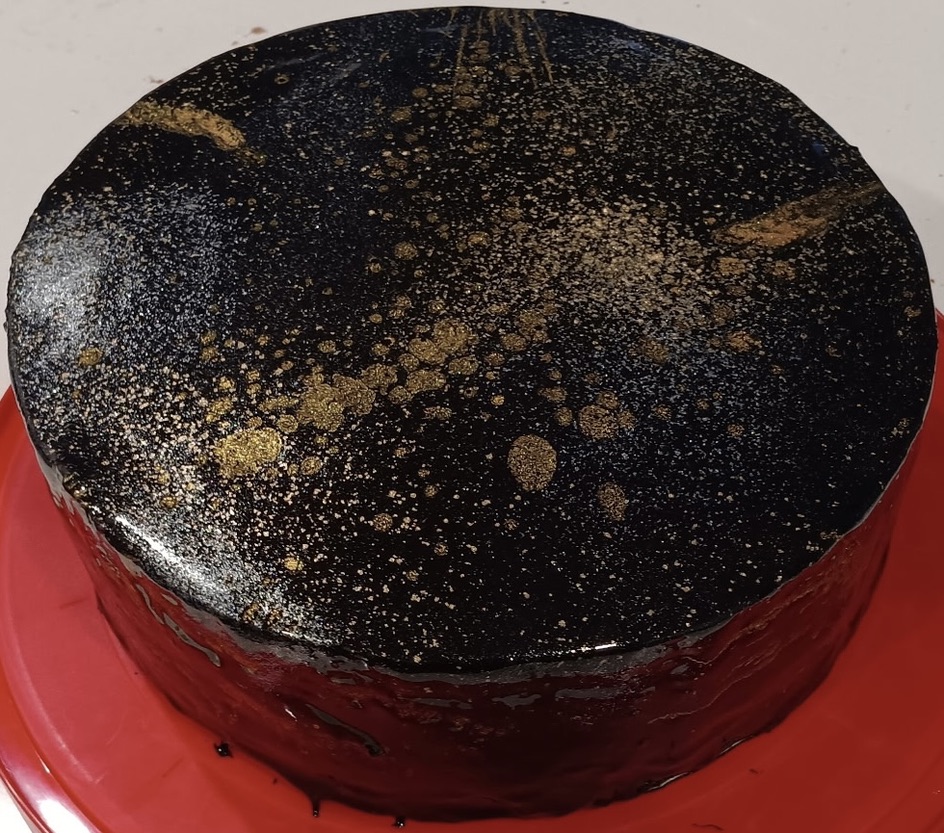 Black mirror-glazed cake with gold-splattered decoration.