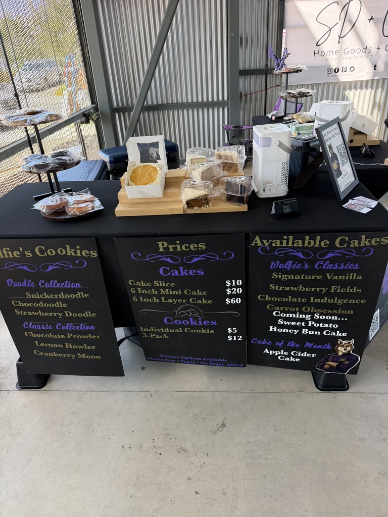 Wolfie’s Cakes booth with cakes, cookies, and menu boards at Hutto Market Days.